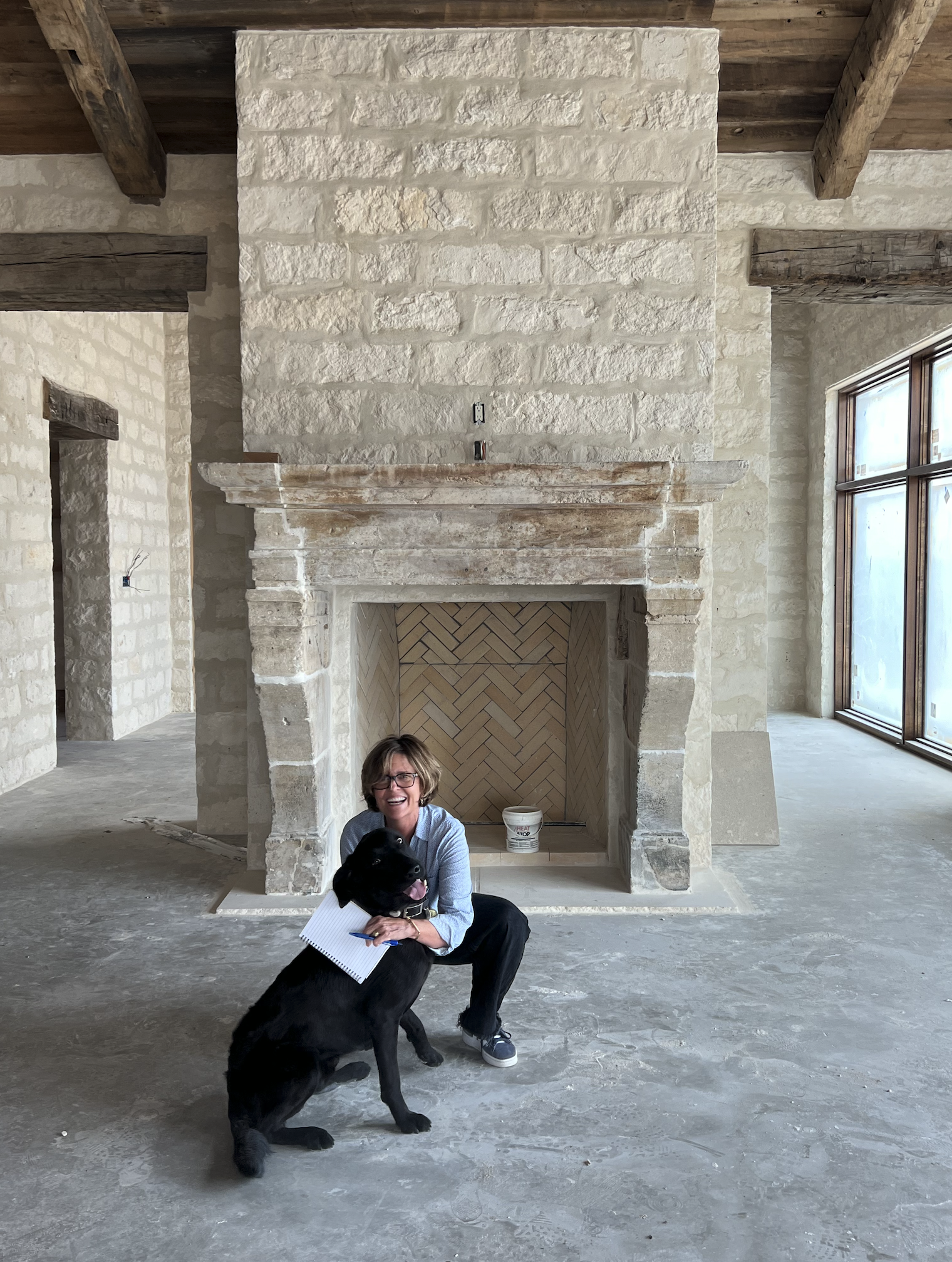 Deborah Kirk on-site at a ranch property, mid-construction, with her dog